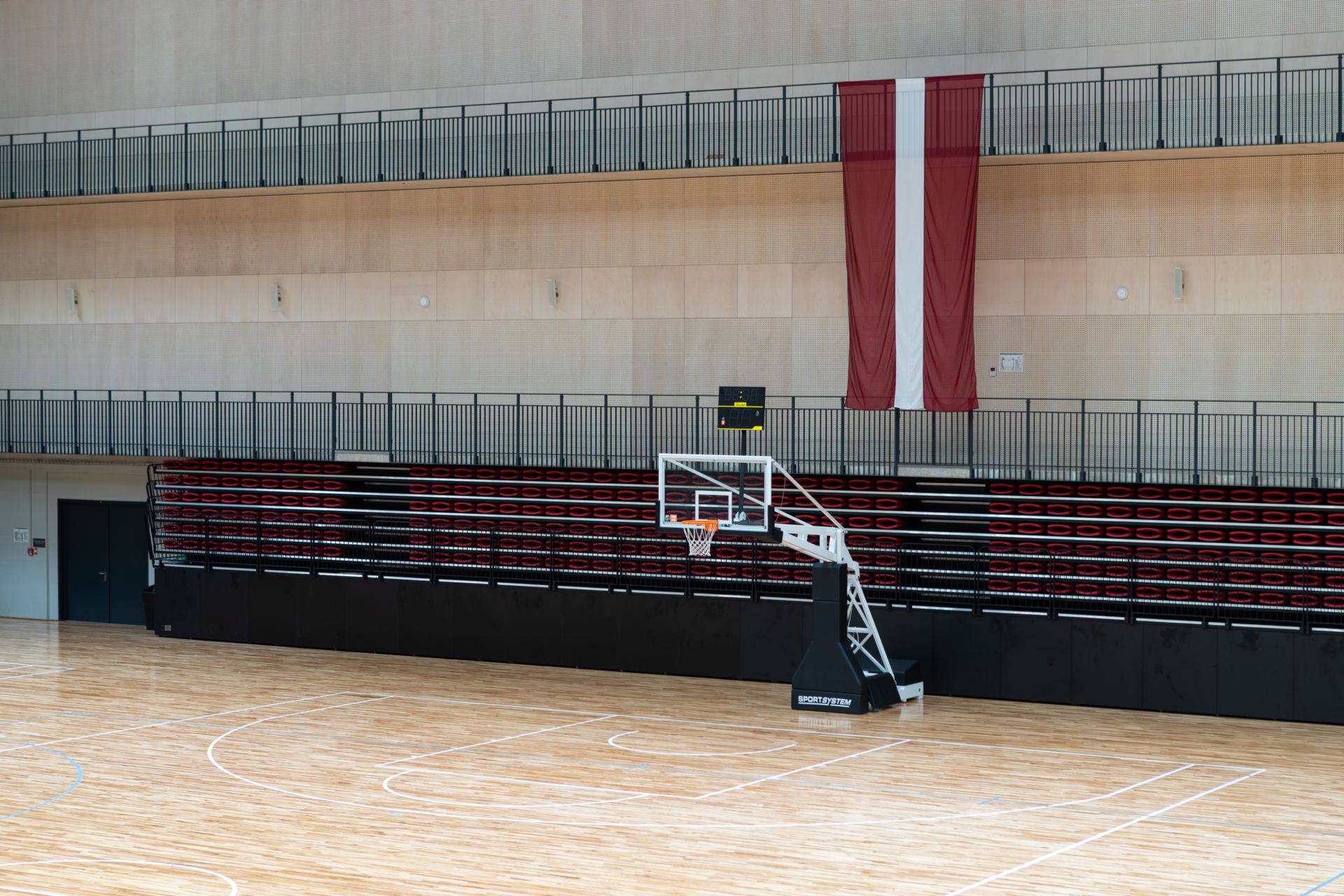 Komandu sporta spēļu halles grozs ar Latvijas karogu fonā